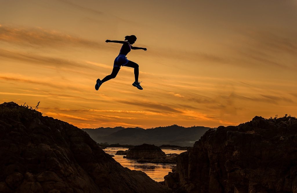 Female athlete jumping across a big gap in sunset demonstrating achievement